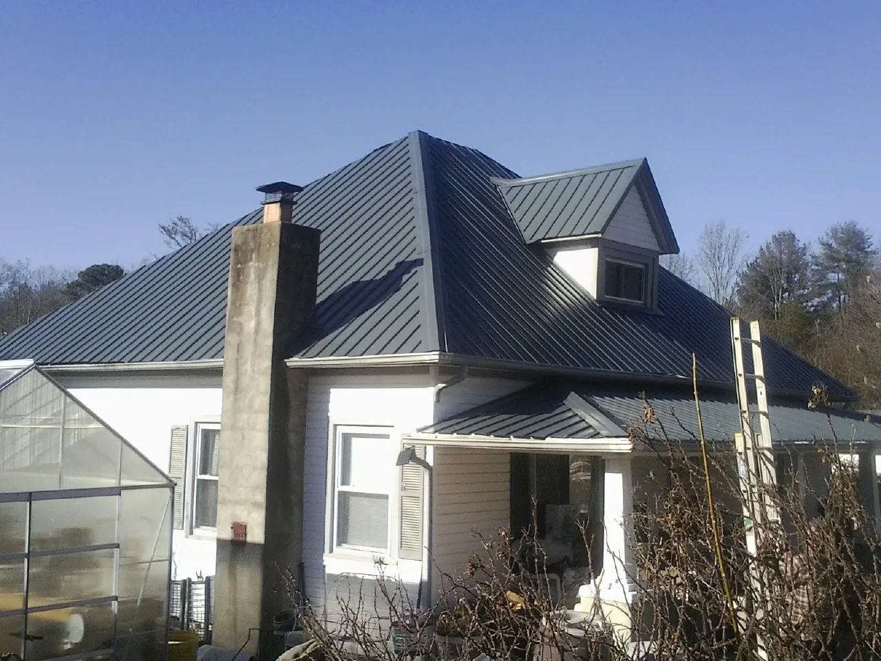 Dark blue standing seam metal roof on a white farmhouse with dormer — Slate & Tile Roof Repair by Roofing Brothers in Pipestone