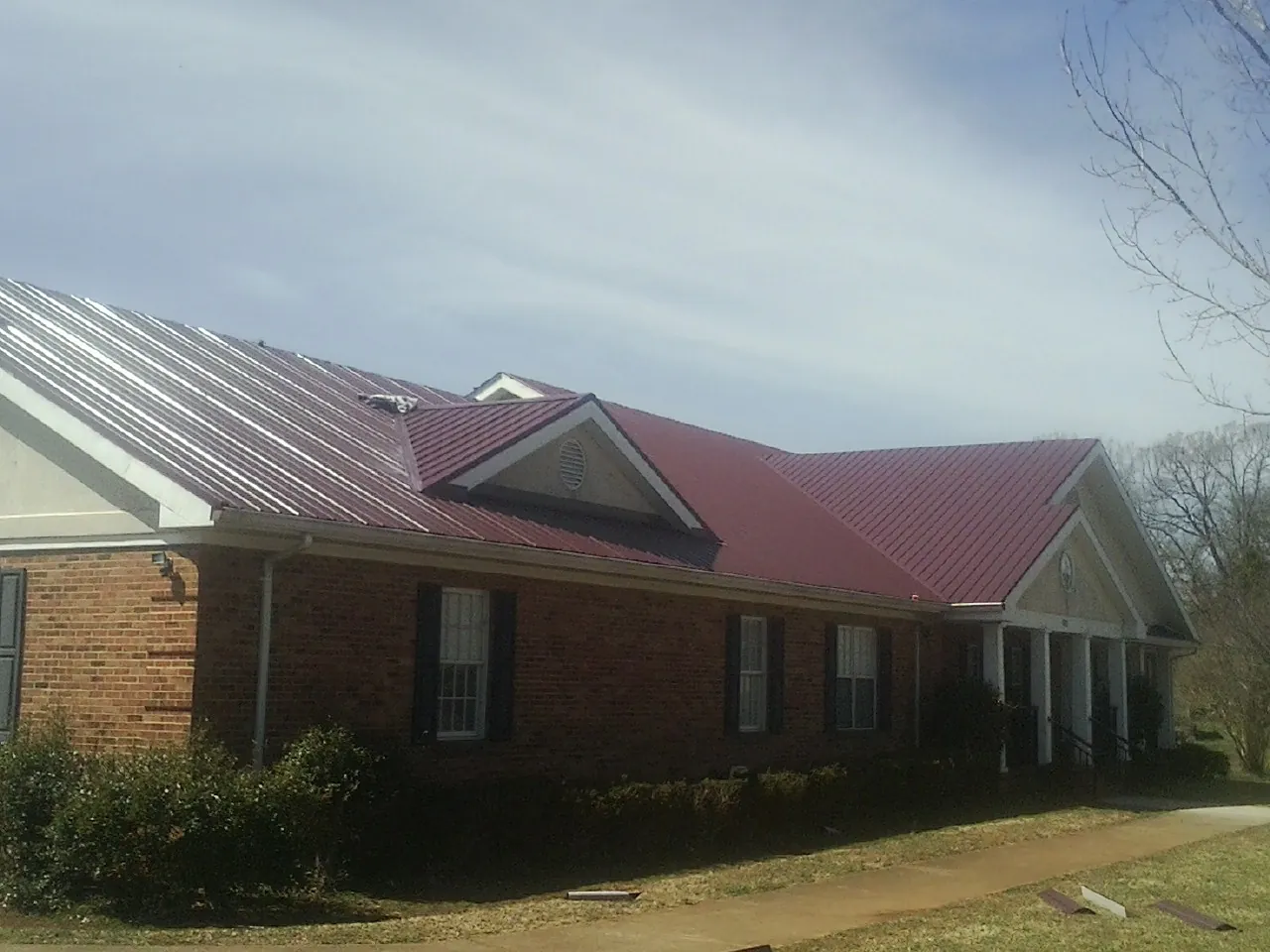 Red metal roof with gabled entries on a long brick building, from a Hail Damage Roof Repair job in Pipestone
