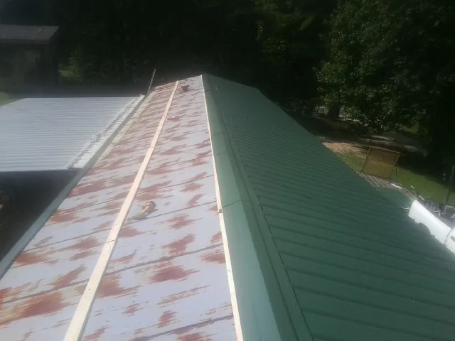 Old rusted panels beside newly installed green metal roofing — Wind Damage Roof Repair by Roofing Brothers in Pipestone