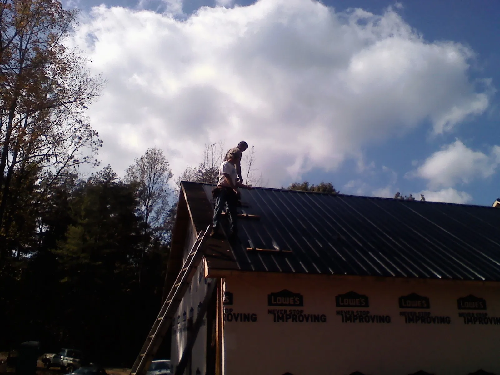 Roofer fastening dark metal panels high against a cloudy sky, from a Roof Inspection job in Pipestone