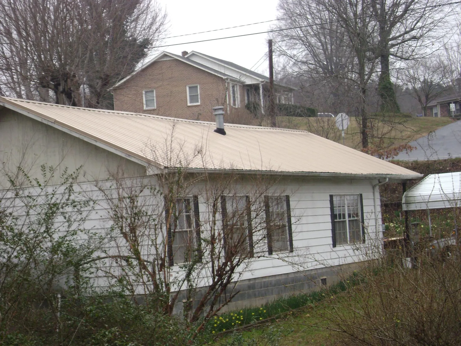Tan metal roof on a white sided house set into a hillside — Commercial Roofing by Roofing Brothers in Pipestone